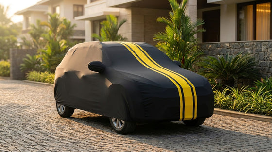 A car parked under a snug black DriveCult body cover with twin yellow stripes in an Indian driveway